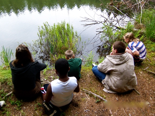 four kids sitting at edge of pond